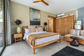 A bedroom with a wooden bed, a sofa, a standing table, and a water dispenser. - Thula Lembongan Villa 5 (Lembongan)