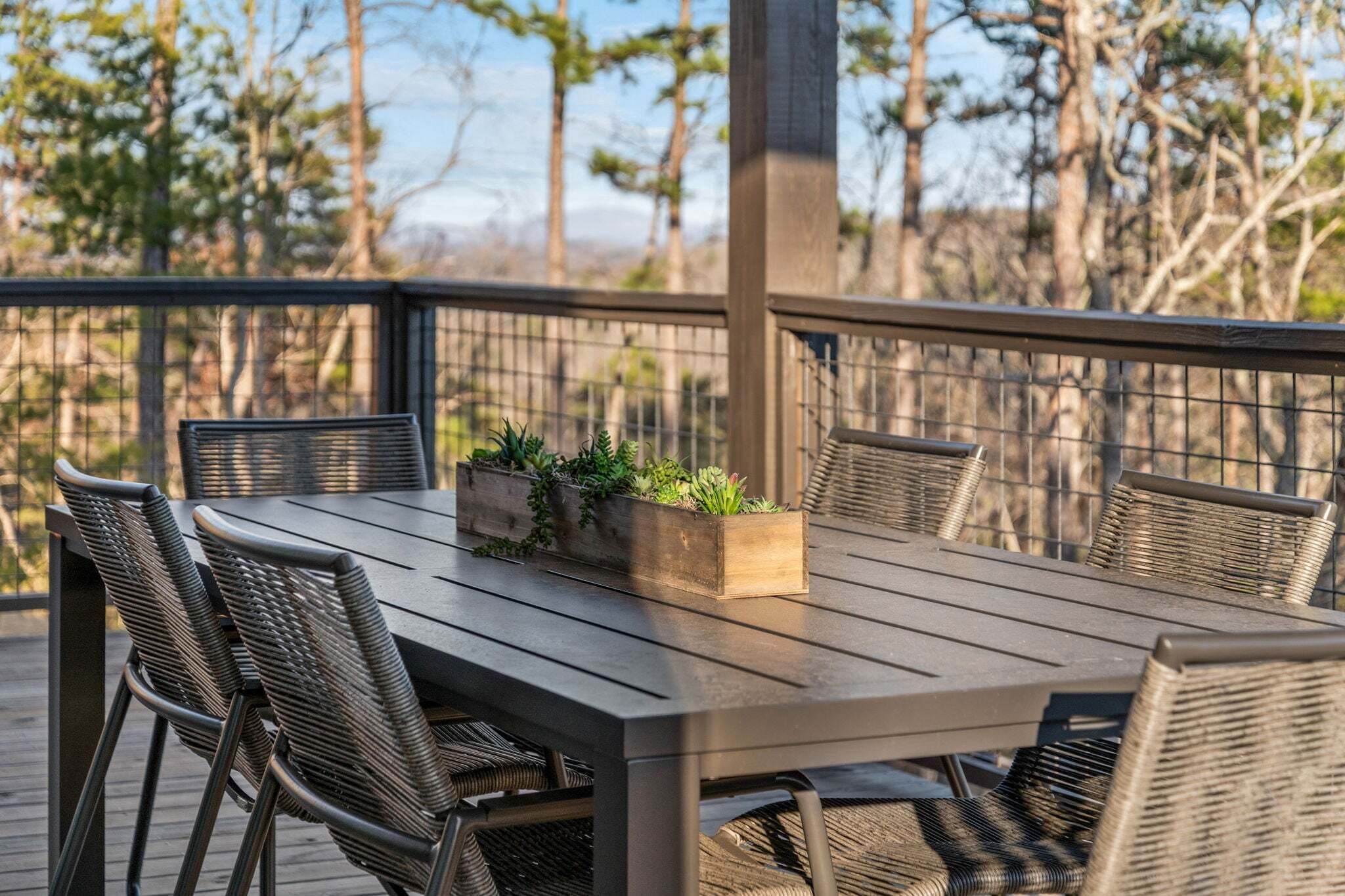 Una terraza al aire libre con una mesa rectangular y cuatro sillas de mimbre, rodeada por una barandilla metálica.