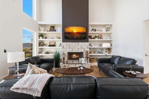 Una sala de estar moderna con chimenea, sofás de cuero negro, una mesa de centro y un televisor montado sobre la chimenea.
