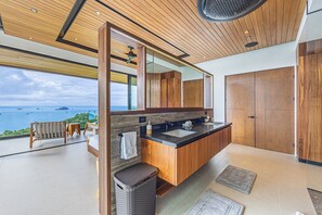 A modern bathroom with a wooden vanity, a large mirror, and a view of the sea. - Ocean View Rainforest Mansion | 10BR, Chef, Cinema & Pools — close to Manuel Antonio National Park (Manuel Antonio)