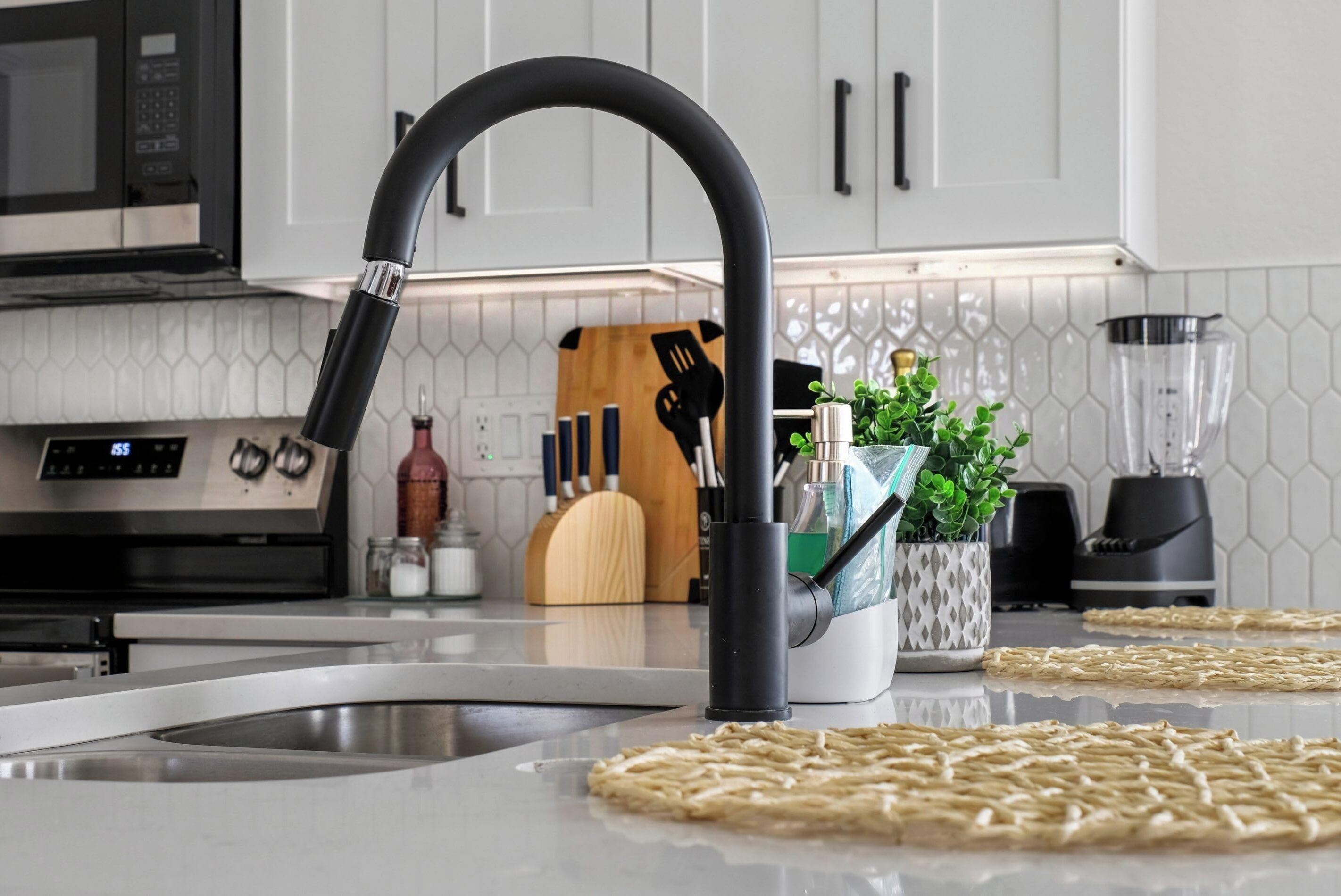 Una cocina con un grifo moderno, un microondas, una estufa y una licuadora sobre la encimera.