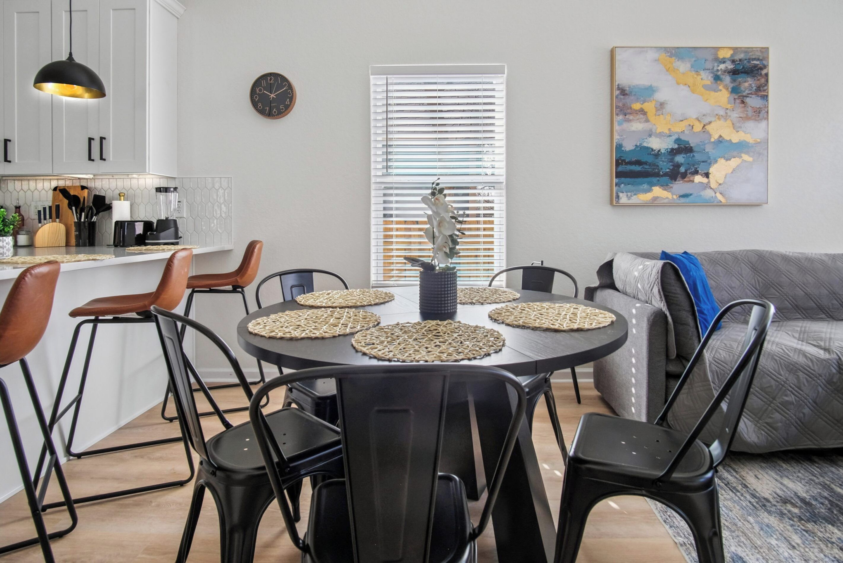 Een eetgedeelte met een ronde tafel, zwarte stoelen en een keuken op de achtergrond.