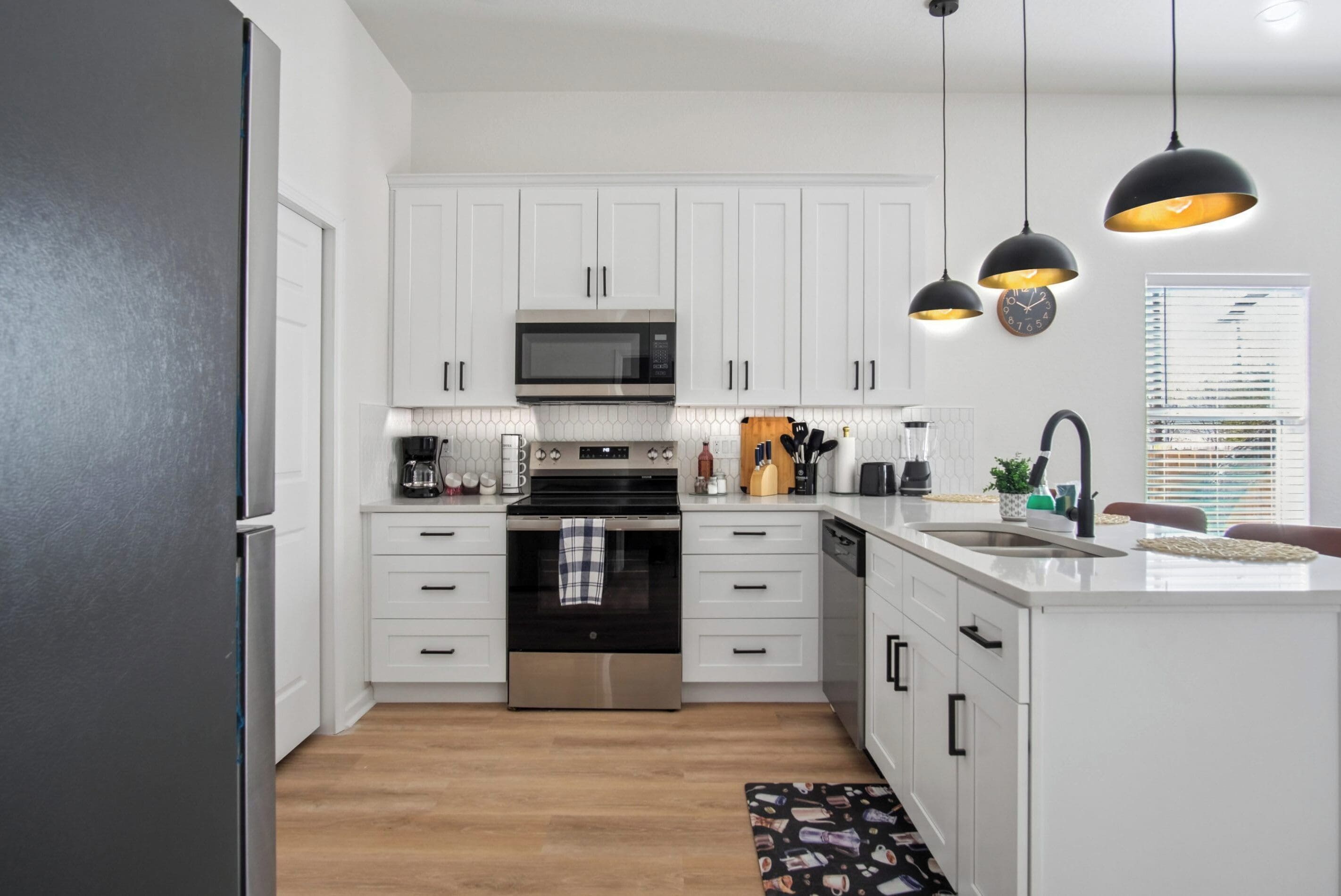 A modern kitchen with white cabinetry, stainless steel appliances, and pendant lighting.