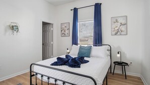 Une chambre à coucher avec un lit, une table de chevet, une fenêtre avec des rideaux et des œuvres d’art murales.