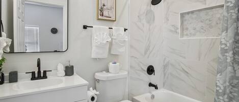 A bathroom with a white sink, toilet, and bathtub. There is a mirror above the sink and a framed picture on the wall.