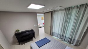 A room with a bed, a piano, a small table with a vase, and a door leading to another room. - Spacious 3BR Brand New Cozy Apt at Dongdaegu KTX Station (Daegu)