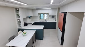 A modern kitchen with white cabinets, a black refrigerator, and a clock on the wall. - Spacious 3BR Brand New Cozy Apt at Dongdaegu KTX Station (Daegu)