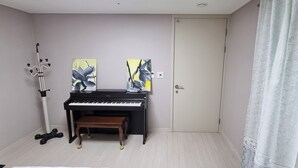 A piano with two paintings, a coat rack, a door, and a patterned curtain. - Spacious 3BR Brand New Cozy Apt at Dongdaegu KTX Station (Daegu)