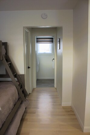 A narrow hallway with a wooden staircase on the left, a door with a towel hanging, and a window with blinds at the end. - Large, modern and comfortable private room (Rimouski)