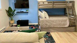 Una cama litera con almohadas, un televisor en la pared, una planta pequeña y un sofá.