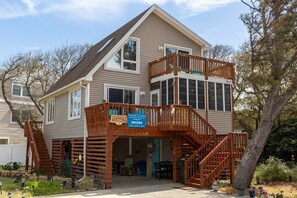 A two-story house with a wooden deck, a covered porch, and a visible garage. - Pookies and Bubbas Cottage: Dog Friendly, Close to the Beach! (Nags Head)