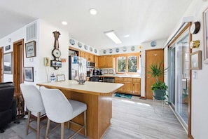 A kitchen with wooden cabinets, a central island, two bar stools, and a potted plant.