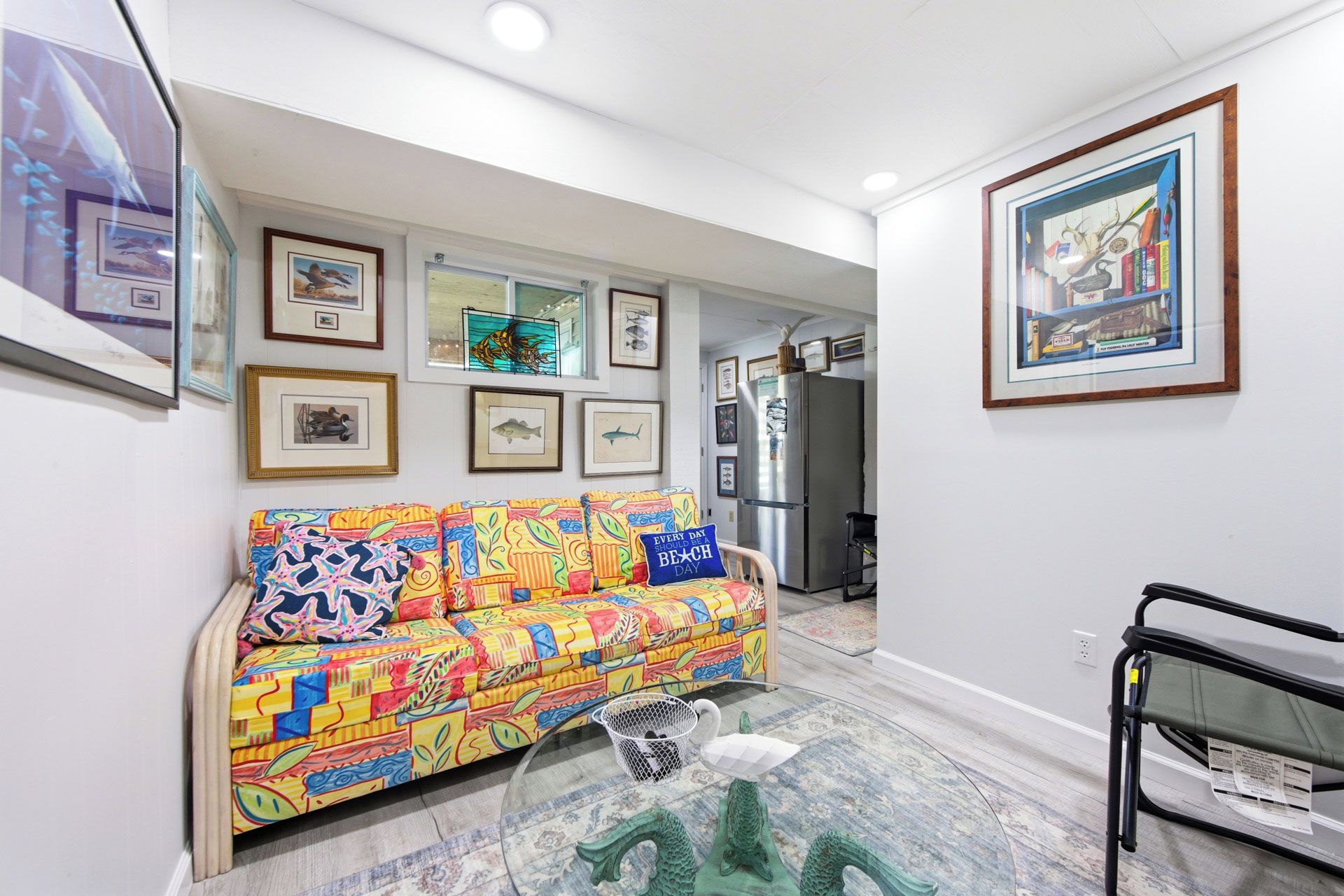 A hallway with a colorful sofa, framed artwork on the walls, and a refrigerator in the background.