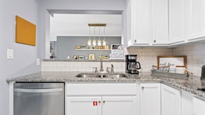 Una cocina moderna con encimera de granito, pileta de acero inoxidable y muebles color blanco.