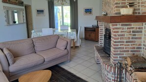 Een woonkamer met een bank, een salontafel, een open haard en een eethoek met een tafel en stoelen.