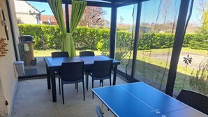 Een overdekt buitengebied met een tafeltennistafel, stoelen en een barbecue.