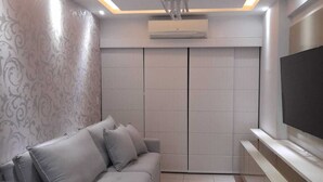 A modern living room with a grey sofa, a flat-screen TV, and a built-in air conditioning unit. - Excellent apartment in Rio2 - Olympic Barra (Rio de Janeiro)