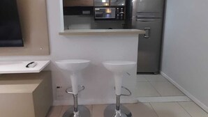 A compact kitchen with a refrigerator, microwave, and a small countertop. There are two stools and a sink. - Excellent apartment in Rio2 - Olympic Barra (Rio de Janeiro)