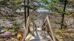 A wooden bridge leading to a rocky shoreline with trees on either side.