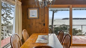 A wooden dining table with chairs, a chandelier, a framed picture, and a view of the sea.