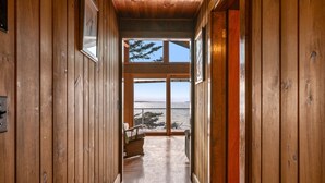 A wooden hallway leading to a large window with a view of the ocean.
