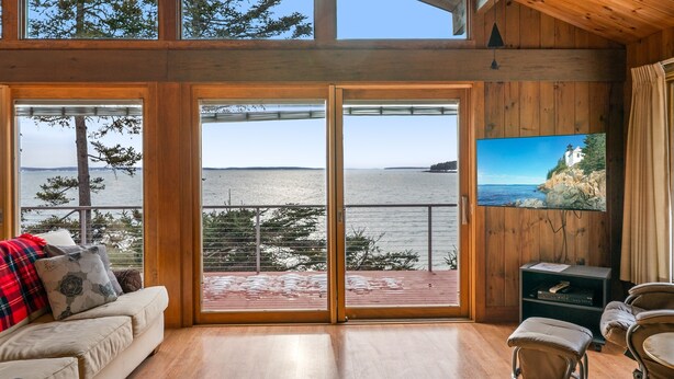 A room with a large sliding glass door leading to a balcony with a view of the water and trees.