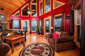A spacious living room with a fireplace, wooden furniture, and large windows. - Smoky Mountain Paradise - Hot Tub Time, Firelit Sips, Game Nights & Summer Swims (Sevierville)
