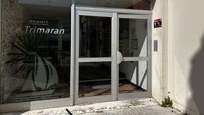 A building entrance with a glass door, a sign reading 'Le Trimaran,' and a small plant on the ground. - Air-conditioned studio by the beach - 3 guests (Port Camargue)
