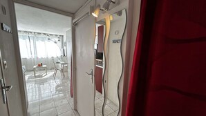 A hallway with a door leading to a dining area, a mirror, and a red curtain. - Air-conditioned studio by the beach - 3 guests (Port Camargue)