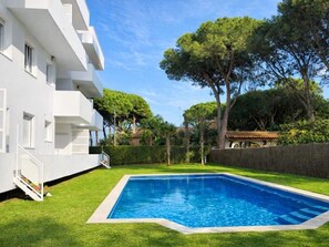 Un bâtiment moderne de couleur blanche, doté d’une piscine rectangulaire entourée d’une pelouse bien entretenue et d’arbres.