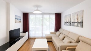 Ein modernes Wohnzimmer mit Flachbildfernseher, weißem Couchtisch, beiger Couch und Holzstuhl.
