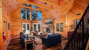Interno di una baita di legno con camino, pavimento in legno, divano e televisione.