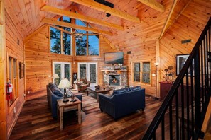 A log cabin interior with a fireplace, wooden floors, a sofa, and a television. - Inspiration Point - Fireside Pet Snuggles, Hot Tub Soaks & Game Nights (Sevierville)