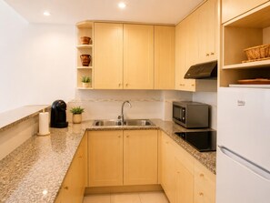 Een moderne keuken met granieten aanrechtbladen, houten keukenkastjes, een ingebouwde magnetron en een koelkast.