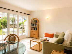 A living room with a glass table, a sofa with cushions, a bookshelf, and a view through large windows. - Apartment near the beach - 2 guests (Palamós)