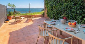 An outdoor dining area with a view of the sea, a tiled patio, and a wall covered in greenery. - Apartment in Palamós - guests (Palamós)