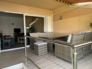 Un balcon doté de meubles en osier, d’un téléviseur et d’une porte-fenêtre coulissante.