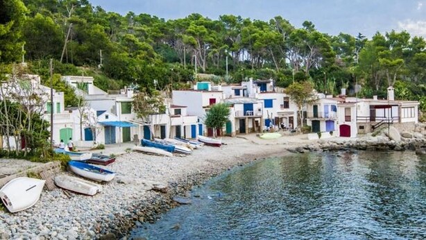 Un pueblo costero con edificios tradicionales, una playa rocosa y barcos.
