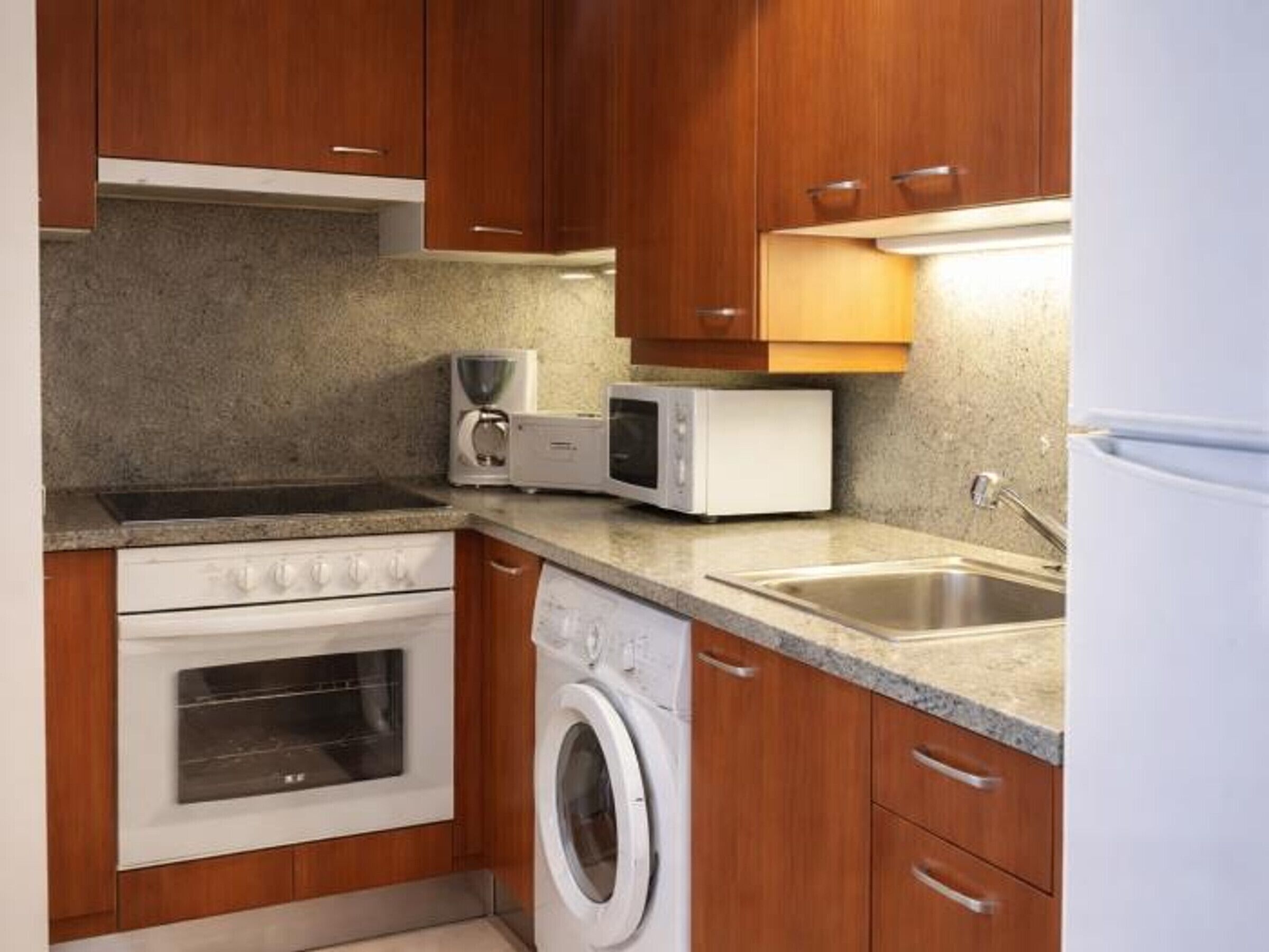 Une cuisine compacte dotée de meubles en bois, d’un four à micro-ondes, d’un grille-pain, d’un évier et d’un lave-linge.