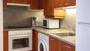 Una cocina compacta con armarios de madera, microondas, tostadora, lavamanos y lavadora.
