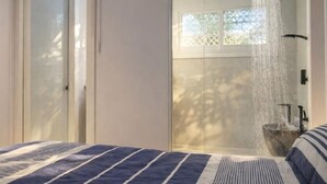 A bedroom with a bed, a shower with a rain showerhead, and a window with a view of trees.
