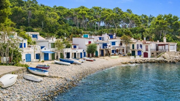A coastal village with white buildings and blue doors, boats on the shore, and a clear blue sky.