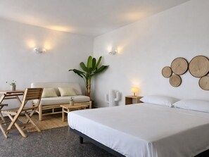 A bedroom with a bed, a sofa, a dining table, chairs, a cactus, wall decor, and a lamp. - Sea view studio La Fosca (Palamós)