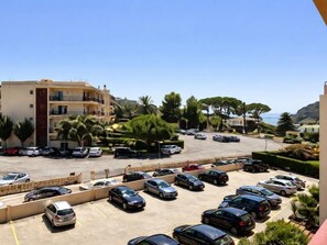 Un pàrquing amb diversos cotxes, un edifici amb balcons i vista al mar.