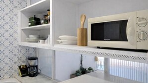 Una cocina con microondas, repisas con vajilla y cafetera.