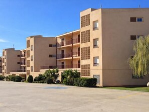 A multi-story residential building with balconies, a parking lot, and greenery. - Sea view studio La Fosca (Palamós)