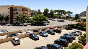 Un estacionamiento con varios autos, un edificio con balcones y vista al mar.