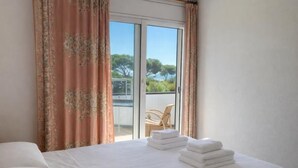 Habitación de hotel con cama, toallas, una silla y vistas a un balcón con otra silla y vegetación.