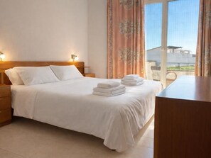 Ein Hotelzimmer mit Bett, Nachttischen, Vorhängen am Fenster und Blick ins Freie.