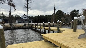 A wooden dock extending into a body of water with a house in the background.